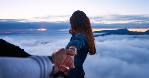 Couple reaching out to the horizon over the clouds.