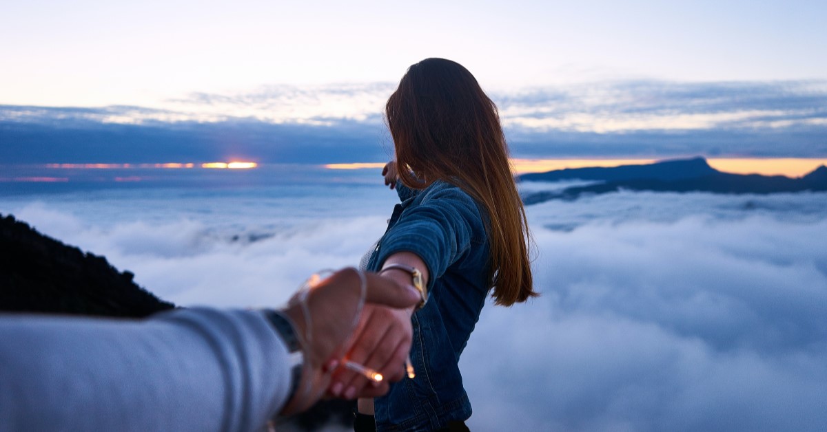 Couple reaching out to the horizon over the clouds