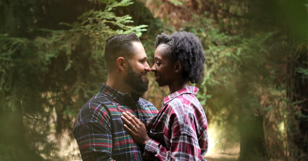 Couple gazing at each other in a forest clearing.